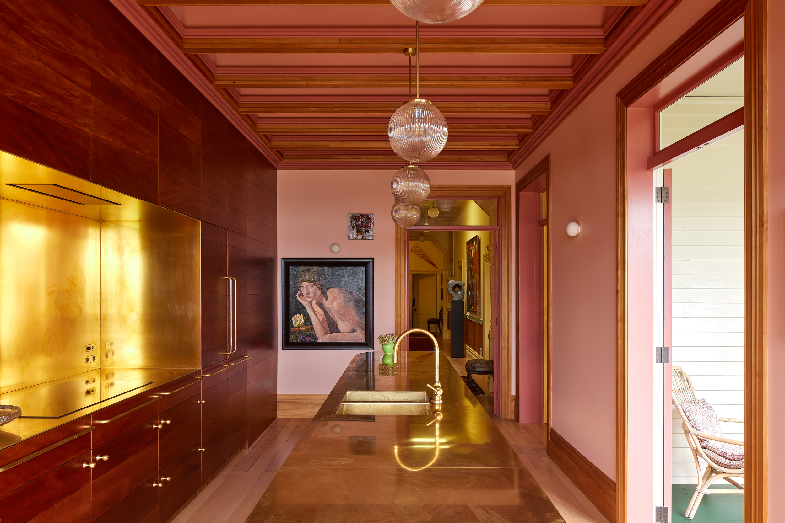 Warm pink and timber kitchen with brass cabinetry and pendant lights