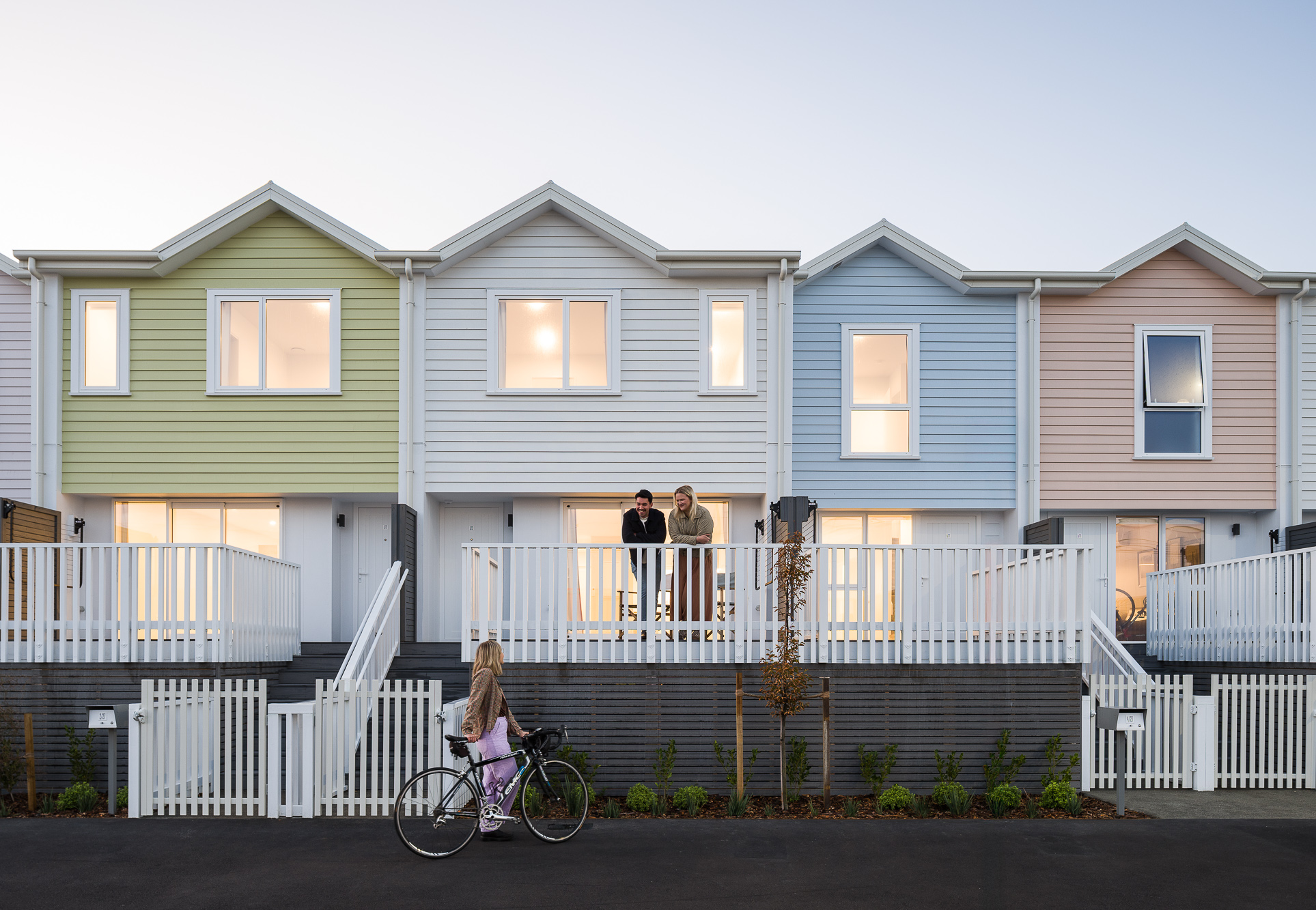 Pastel townhouses with residents on balconies and a cyclist passing by